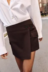 Falda pantalón cruzada de color marrón oscuro, con diseño tipo cargo que incluye bolsillos laterales con solapa y botones decorativos en la cintura.