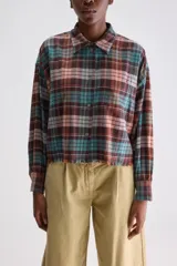 Camisa de algodón con estampado de cuadros estilo tartán en tonos marrón, turquesa y rosado. Presenta un calce relajado y largo cropped, cuello clásico, hombros caídos, bolsillo aplicado en el frente y mangas amplias con puños ajustados. El ruedo cuenta con terminación desflecada.