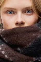 Bufanda de tejido suave con acabado cepillado, diseño de rombos tipo argyle en tonos marrón y negro, y flecos en los extremos.