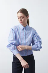 Camisa de manga larga a rayas verticales azules y rojas, con cuello clásico, cierre frontal de botones y mangas abullonadas con puños ajustados.