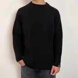 Sweater de tejido de punto grueso en color beige, con cuello redondo y mangas raglán. Presenta un diseño holgado y una pequeña etiqueta con logo en el puño.