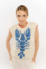 Chaleco tejido a mano en lana merino, color beige con diseño de langosta en color azul y detalles de terminación en rojo en cuello y sisas.