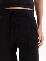 Pantalón tipo babucha de color negro, con cintura elástica y cordón de ajuste, bolsillos laterales y costuras verticales decorativas en el frente.