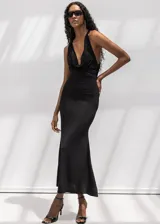 Vestido largo negro de corte al cuerpo, con escote halter y cuello drapeado. Presenta una silueta entallada que se ensancha suavemente hacia el ruedo.