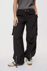 Pantalón cargo negro de corte relajado y pierna ancha con bolsillos laterales con solapa, cintura con doble broche y cierres metálicos en los tobillos.