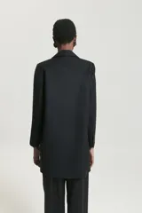 Saco largo sastrero negro de lana fría, corte recto, con cuello y solapa, botones en el delantero y en los puños.