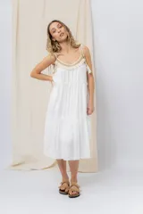 Vestido largo blanco de algodón con escote en V, breteles finos regulables con lazo y borlas, y detalle de tejido artesanal en el escote.