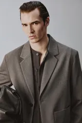 Blazer de corte relajado en color marrón oscuro, con cuello de solapas de muesca, cierre frontal de dos botones y bolsillos de plastrón en la parte delantera.