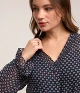 Vestido corto azul marino con estampado de flores blancas y rojas, escote en V, mangas largas con puños elásticos y falda con volantes. Incluye cinturón negro con hebilla dorada.