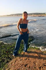 Top corto de denim azul con estampado de monogramas, escote recto, breteles finos y cierre en la espalda.