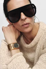 Pulsera rígida de metal con acabado texturizado y labrado en tono dorado, con una aplicación central circular incrustada de cristales negros brillantes.