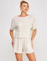 Blusa corta de lino y viscosa color beige, con bordado de grandes flores al tono, cuello redondo, mangas cortas abullonadas y corte holgado.