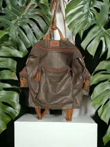 Mochila grande de cuero color gris con herrajes color bronce. Tiene doble asa de mano y correas traseras regulables.