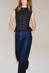 Chaleco de denim azul oscuro con cuello redondo y cierre frontal de botones. Presenta un diseño de pespuntes decorativos en contraste con forma de alamares en la parte delantera.
