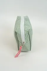 Neceser de tela con estampado de cuadros vichy en color verde y blanco. Cuenta con una etiqueta frontal con el logo de la marca y un tirador de cierre en color rosado.