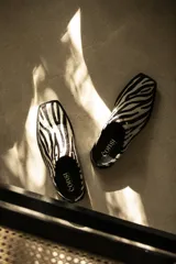 Suecos chatos de cuero con estampado animal print de cebra, punta cuadrada y detalles de tachas metálicas en los laterales.