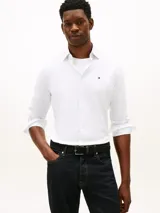 Camisa blanca de corte regular de Tommy Hilfiger, confeccionada en puro algodón regenerativo con diseño de raya diplomática y sutil textura diagonal. Presenta cuello camisero, cierre frontal de botones y el logo de la marca bordado en el pecho.
