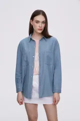 Sobrecamisa celeste de denim con cuello camisero, cierre frontal con botones a presión, dos bolsillos con solapa en el pecho y mangas largas con puños abotonados.