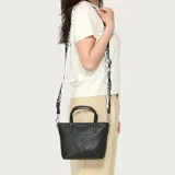 Cartera Guess modelo Keira en color negro, con diseño texturizado, doble asa superior y correa ajustable de tela con estampado de la marca en blanco y negro. Incluye un parche triangular con el logo de la marca en la parte frontal y herrajes metálicos plateados.