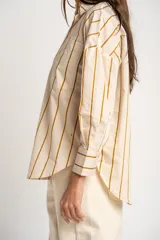 Camisa de corte oversize con estampado de rayas verticales en tonos verde, blanco y ocre. Presenta cuello clásico, cierre frontal con botones, bolsillo en el pecho y mangas largas con puños abotonados.