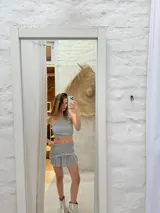 Top de un solo hombro, color gris claro, confeccionado en tela acanalada con brillo y apliques de tachuelas plateadas.