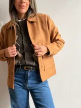 Chaqueta de estilo clásico con acabado efecto gamuza, confeccionada en algodón. Presenta cierre frontal con botones, cuello camisero y dos bolsillos delanteros con solapa. Posee interior forrado y corte recto.