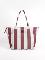 Bolso tipo tote grande, resistente al agua, con diseño de rayas verticales rojas y blancas. Cuenta con asas largas de hombro, cierre superior y parche de cuero con logo grabado. Incluye neceser transparente a juego con base y detalles a rayas.