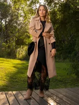 Trench color beige con doble botonadura, cuello clásico, solapas de muesca, cinturón y bolsillos laterales.