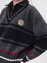 Pullover de punto con textura aterciopelada, diseño oversize, cuello polo con cierre frontal parcial y detalles de pespuntes en contraste. Presenta rayas horizontales en tonos tierra y un parche bordado con la letra M en el pecho.