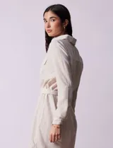 Vestido camisero corto a rayas verticales celestes y blancas, con cuello con solapa, abertura frontal con botones, dos bolsillos de parche en el pecho y lazo de ajuste en la cintura.