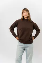 Sweater de tejido de punto color marrón, con cuello alto, corte relajado y terminaciones en rib en puños y cintura. Presenta una hilera de botones metálicos decorativos en uno de los laterales.