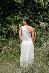 Conjunto blanco de lino, compuesto por un top sin mangas con un solo hombro y detalle de calado, y una falda larga con aberturas frontales y detalle de calado.