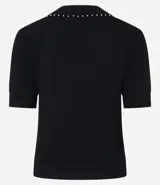 Blusa negra de punto con cuello polo, escote en V y mangas cortas. Detalle de mini perlas aplicadas en el cuello.