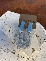 Aros largos colgantes de diseño estructurado, compuestos por una base rectangular metálica lisa, una cuenta facetada plateada y flecos formados por múltiples tiras de strass brillante.