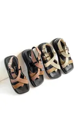 Sandalias de plataforma con diseño de tiras cruzadas en el empeine, puntera cuadrada y cierre de hebilla ajustable en el tobillo. Presentan una combinación de texturas en cuero y gamuza con suela de goma negra.