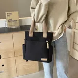 Cartera tipo shopper color beige con bolsillos laterales y un bolsillo frontal con tirador de cordón trenzado. Cuenta con asas superiores de lona.