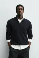 Jersey de punto regular fit, color negro, con cuello perkins y cierre frontal de cremallera. Presenta manga larga y acabados en rib.