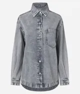 Camisa de corte oversized confeccionada en denim de algodón con lavado gris desgastado. Presenta cuello clásico, cierre frontal con botones metálicos, manga larga con puños abotonados y un bolsillo aplicado en el pecho. El diseño incluye un bajo redondeado.