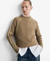 Sweater de punto color beige, con cuello alto y diseño de manga larga raglán con detalle de línea blanca lateral. Presenta un tejido acanalado y corte recto.