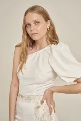 Top blanco con un hombro descubierto y manga abullonada.