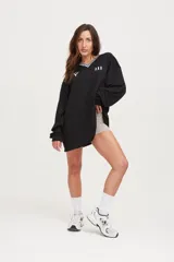 Camiseta negra oversize de manga larga con cuello en V blanco y logo en el pecho.