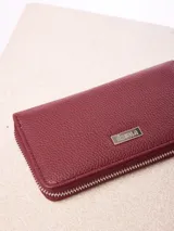 Billetera Rusty modelo Novadi W26, de color bordó con textura granulada, cierre perimetral de cremallera y placa metálica con la marca grabada en el frente.