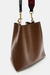 Bolso de hombro tipo saca en color marrón, con diseño minimalista y cierre de clip metálico. Incluye una correa de hombro con detalles troquelados en contraste y herrajes dorados.