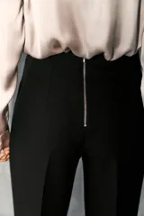 Pantalón de tiro alto en color negro, con diseño de corte recto y ligeramente acampanado. Presenta costuras verticales marcadas en el frente y bolsillos laterales de vivo.