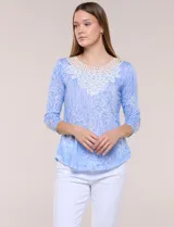 Blusa celeste con estampado floral devoré, de manga tres cuartos, escote redondo amplio y detalle de pechera de encaje blanco en contraste.