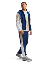 Pantalón deportivo Under Armour modelo Rival Woven CB Pants, de corte recto en color azul marino con franjas laterales en color beige y blanco, cintura elástica y tecnología UA Storm repelente al agua.