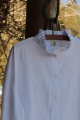 Camisa blanca de lino con cuello alto con volados y mangas largas.