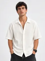 Camisa de manga corta color blanco, de corte holgado y tejido texturizado con cierre frontal de botones.