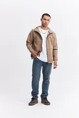 Campera con capucha y cierre frontal, color beige, con detalles de costuras y cierres en negro. Presenta mangas largas con puños acanalados y logo pequeño en el pecho.