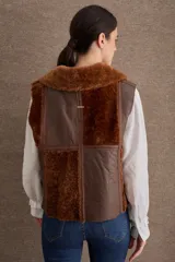 Chaleco de cuero y piel sintética en color marrón, con diseño de paneles combinados, cuello solapa y cierre frontal con cremallera.